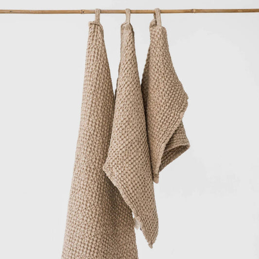 Beige vaffelvevd linhåndkle som henger på en snor på badet