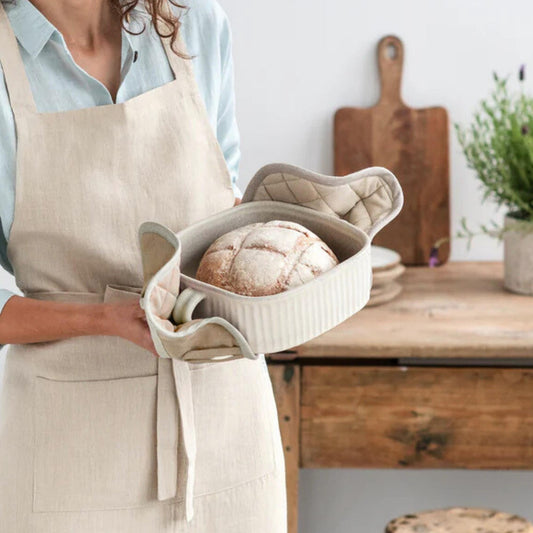 Dame holder en form med hjemmelaget brød med beige gryteklut i lin – bærekraftige og naturlige kjøkkentekstiler