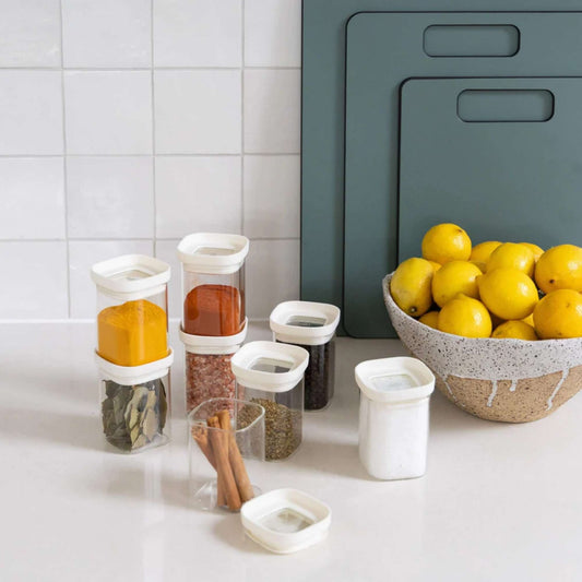 Krydderglass i glass med glasslokk fylt med krydder som gurkemeie, paprika og pepper organisert på kjøkkenbenk.