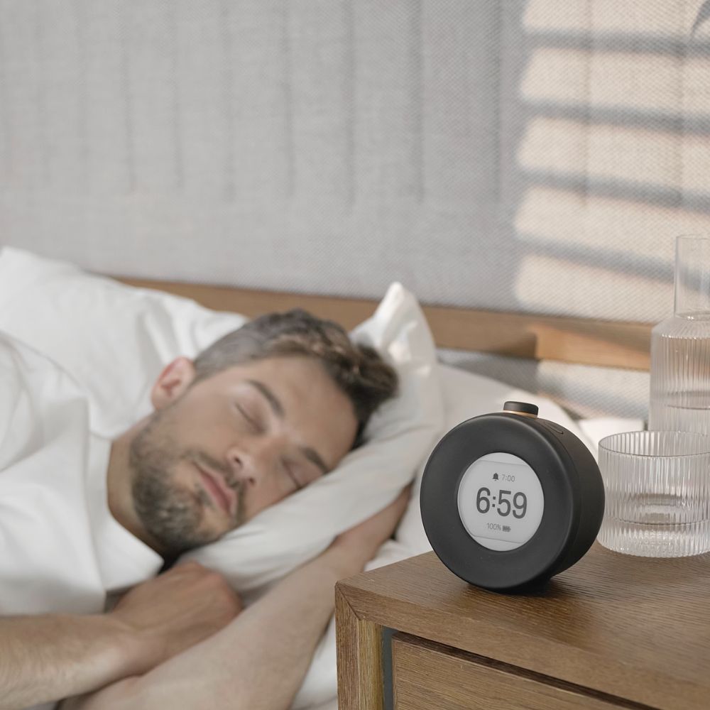 Mann med lav EMF-alarmklokke med redusert blått lys på nattbordet for et sunnere sovemiljø.