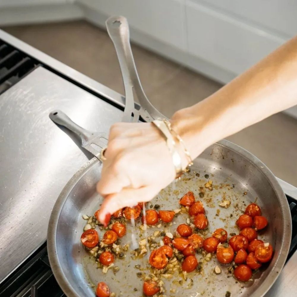 Nikkelfri Lil Flippa stekespade i rustfritt stål brukt sammen med stekepanne med tomater. Trygt kjøkkenredskap som tåler syrlige råvarer uten å frigjøre uønskede stoffer.