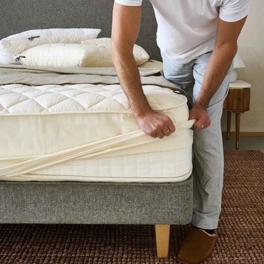 Mann legger på madrassbeskytter laget av ren britisk ull for sunnere søvn og et naturlig, bærekraftig hjem