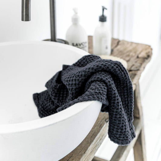 Mørkegrått håndkle i lin og bomull plassert på baderom med naturlige detaljer. Vaffelstruktur gir en luksuriøs spa-følelse og bidrar til et sunt og friskt hjemmemiljø