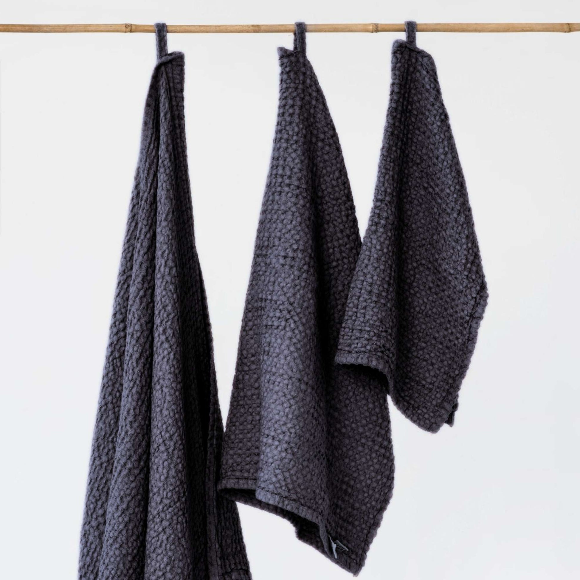 Tre mørkegrå håndklær i lin og bomull fra MagicLinen lagt ved siden av hverandre, viser de ulike størrelsene og den myke vaffelstrukturen.