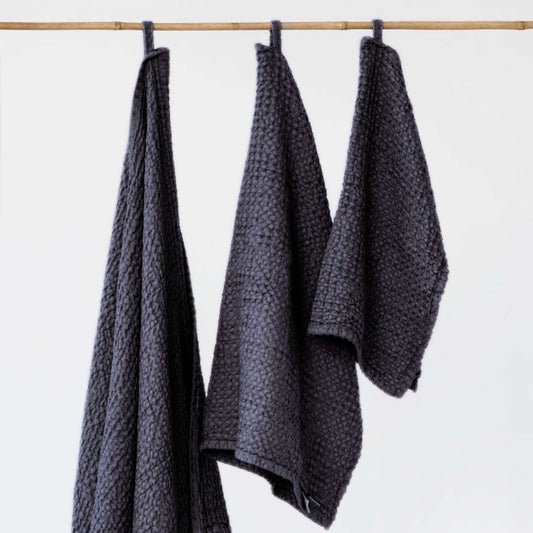 Tre mørkegrå håndklær i lin og bomull fra MagicLinen lagt ved siden av hverandre, viser de ulike størrelsene og den myke vaffelstrukturen.