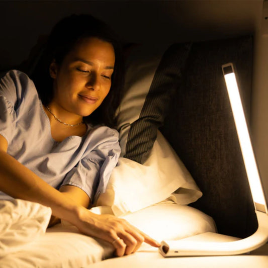 Kvinne bruker Oculamp med varmt kveldslys på nattbord i soverom