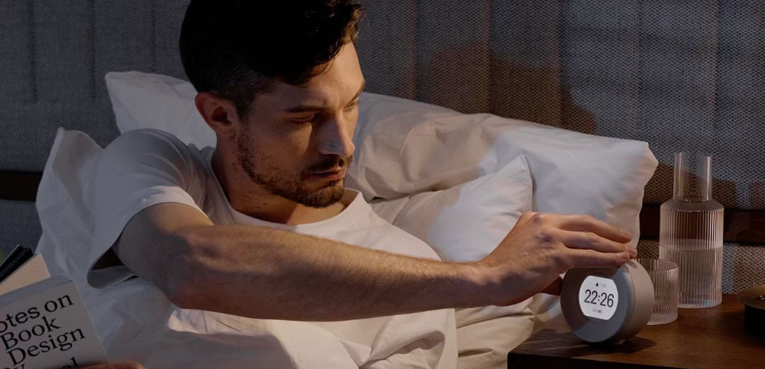 Mann sover rolig i teknologifritt soverom med Mudita vekkerklokke på nattbordet