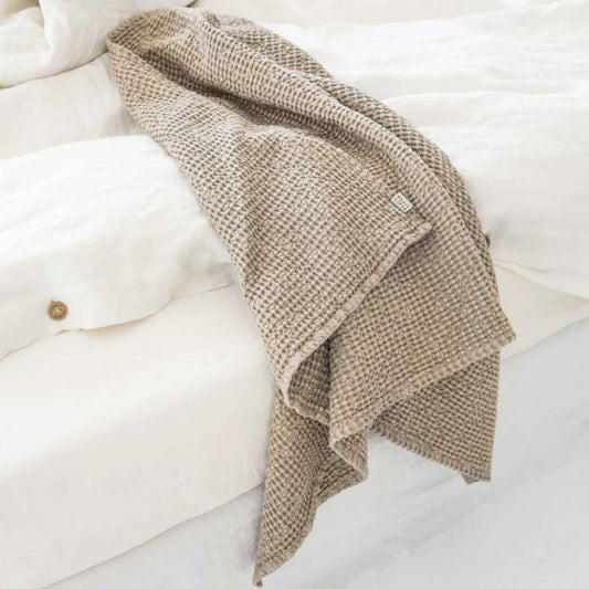 Naturlig beige håndkle i lin og bomull på seng med lin sengetøy, viser bærekraftige materialer og et sunt, miljøvennlig hjem.