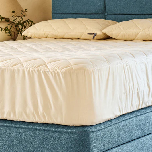 Madrassbeskytter i ull og bomull lagt på seng, laget av naturlige materialer og brukt under laken for et mer pustende sovemiljø.