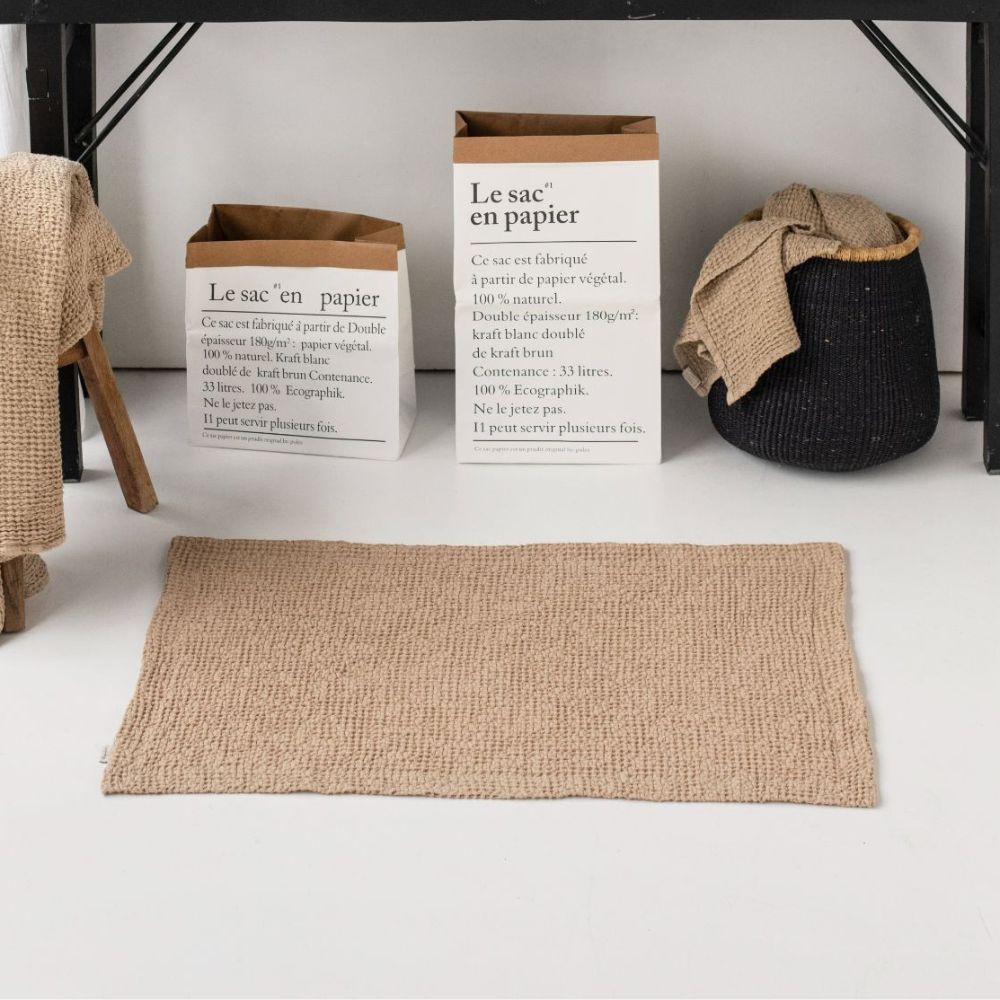 Badematte i vaffelvevd lin og bomull i fargen beige, liggende på baderomsgulv