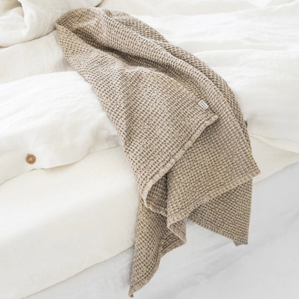Beige badehåndkle i lin og bomull lagt på en seng med lin sengetøy, naturlige materialer som gir en bærekraftig og allergivennlig følelse for et sunt hjem.