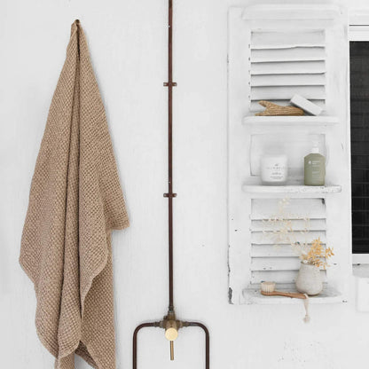 Beige badehåndkle i vaffelvevd lin plassert på et naturlig bad med lyse toner, treverk og en rolig, luksuriøs spa-følelse.