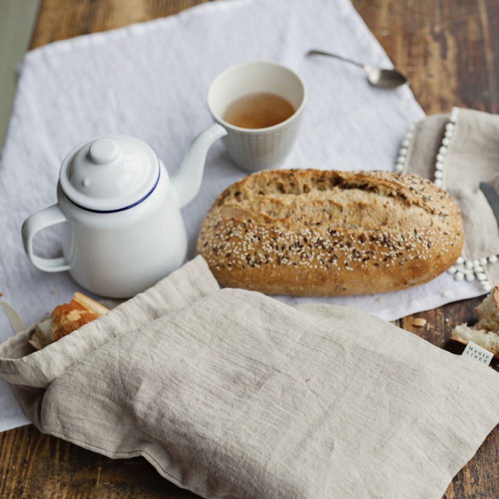 Brød i naturfarget linpose fra MagicLinen på kjøkkenbord sammen med ferskt brød