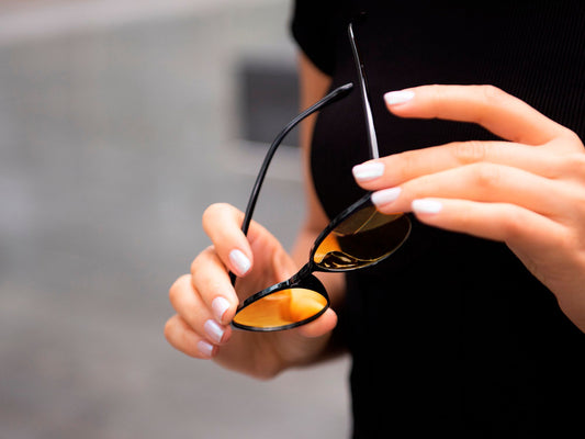 Damehånd som holder Ocushield Carson blålysbriller med sort innfatning og oransje glass