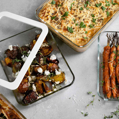 Firkantede glassbeholdere i borosilikatglass med glasslokk fylt med ovnsbakte grønnsaker og pastaform. Plastfri matoppbevaring på kjøkkenbenk.