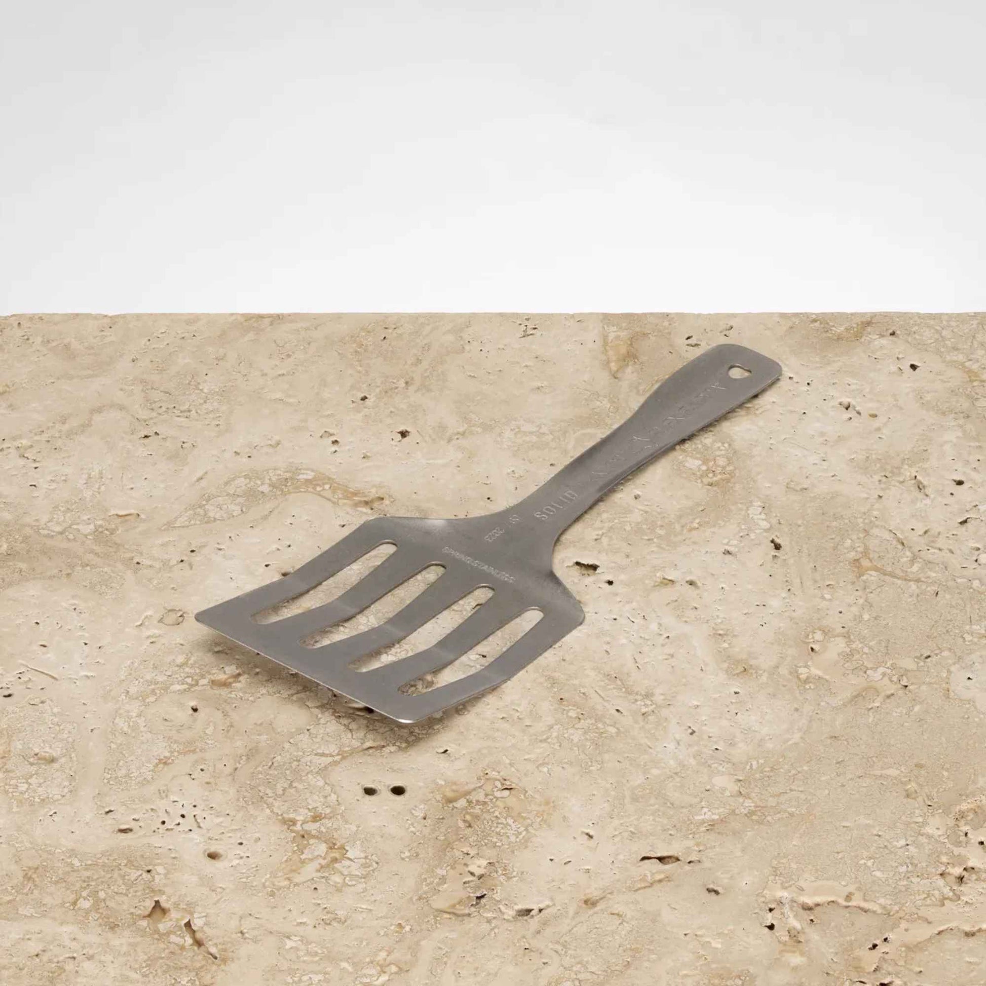 Flexi Flippa stekespade i rustfritt stål fra Solidteknics på steinbenk. Plastfri stekespade laget av ett solid stykke rustfritt fjærstål.