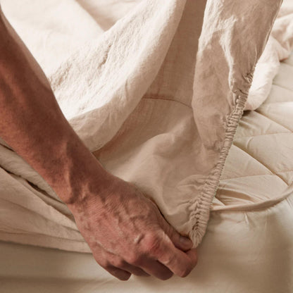 En mann legger på Mariana stretchlaken i økologisk bomull og lin i fargen sand, viser den elastiske kanten som gir perfekt passform