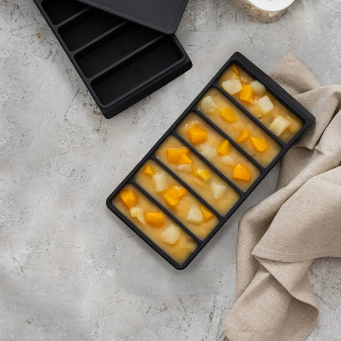 Fryseform i LFGB-sertifisert platinumsilikon med seks 100 ml rom, fylt med porsjonsfrosne fruktbiter. Perfekt til babymat, sauser og små porsjoner – plastfritt alternativ fra Sunnere Hjem.