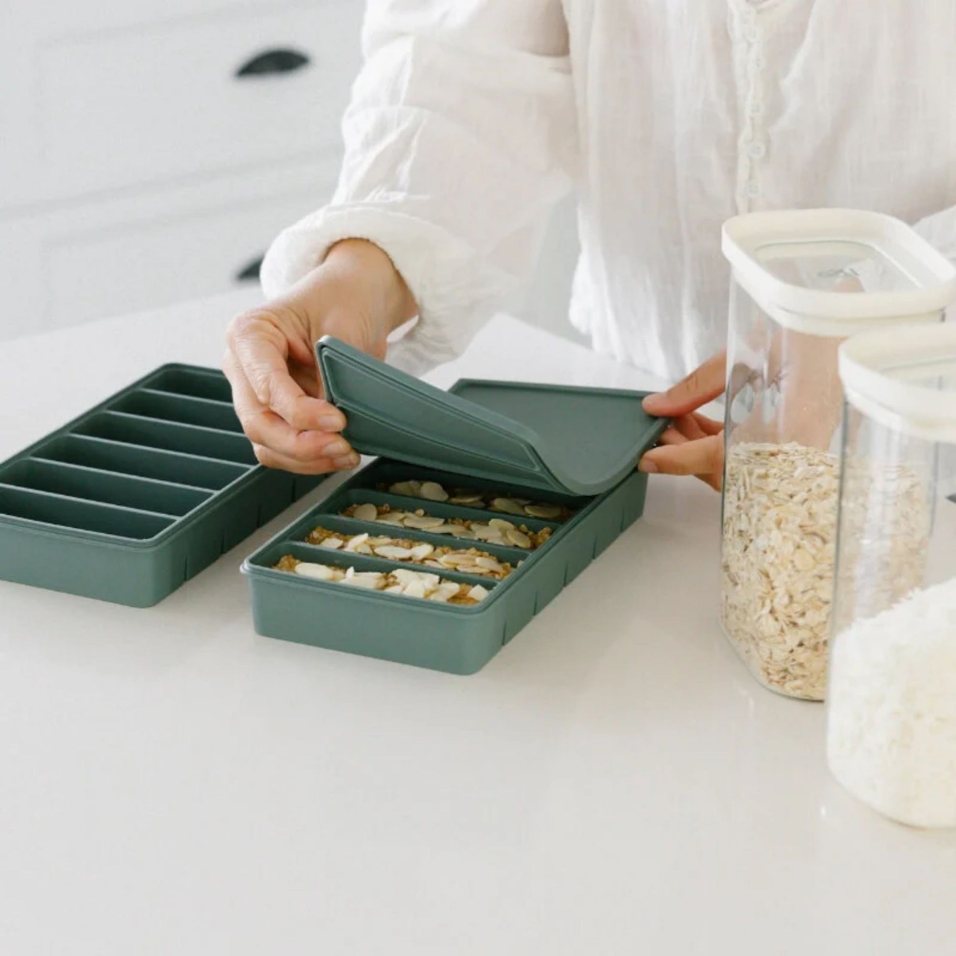 Person åpner silikon fryseform med seks 100 ml rom fylt med porsjoner, laget i LFGB-sertifisert silikon fra Seed & Sprout.