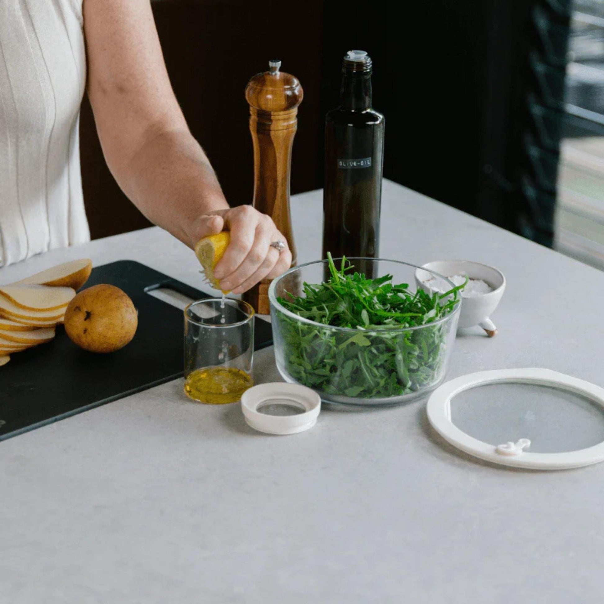 Rund borosilikatglassbeholder fylt med frisk salat på kjøkkenbenk, med glasslokk og silikonforsegling ved siden av.