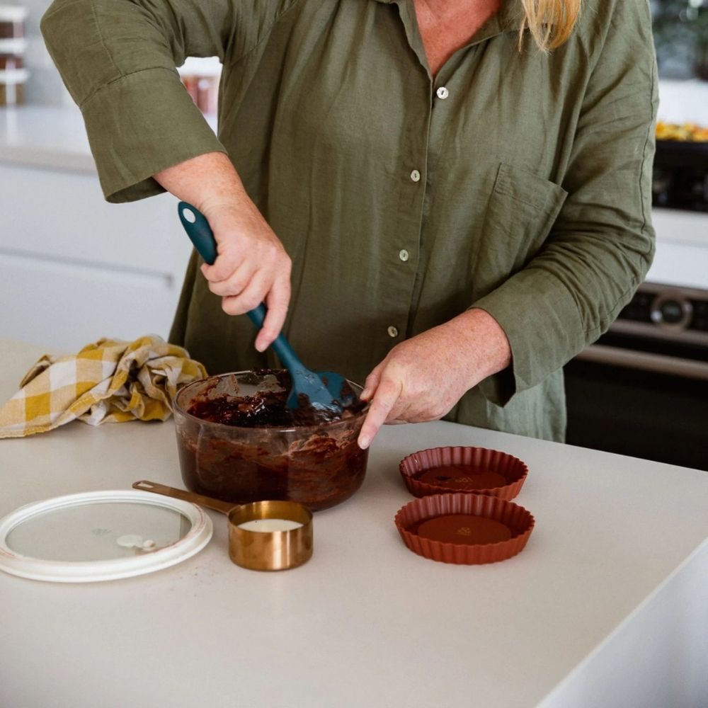 Person som rører i en glassbeholder fra Seed & Sprout på kjøkkenbenken, omgitt av silikonformer og målebeger.