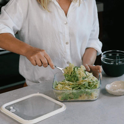 Person serverer pesto­pasta fra en rektangulær glassbeholder med glasslokk.