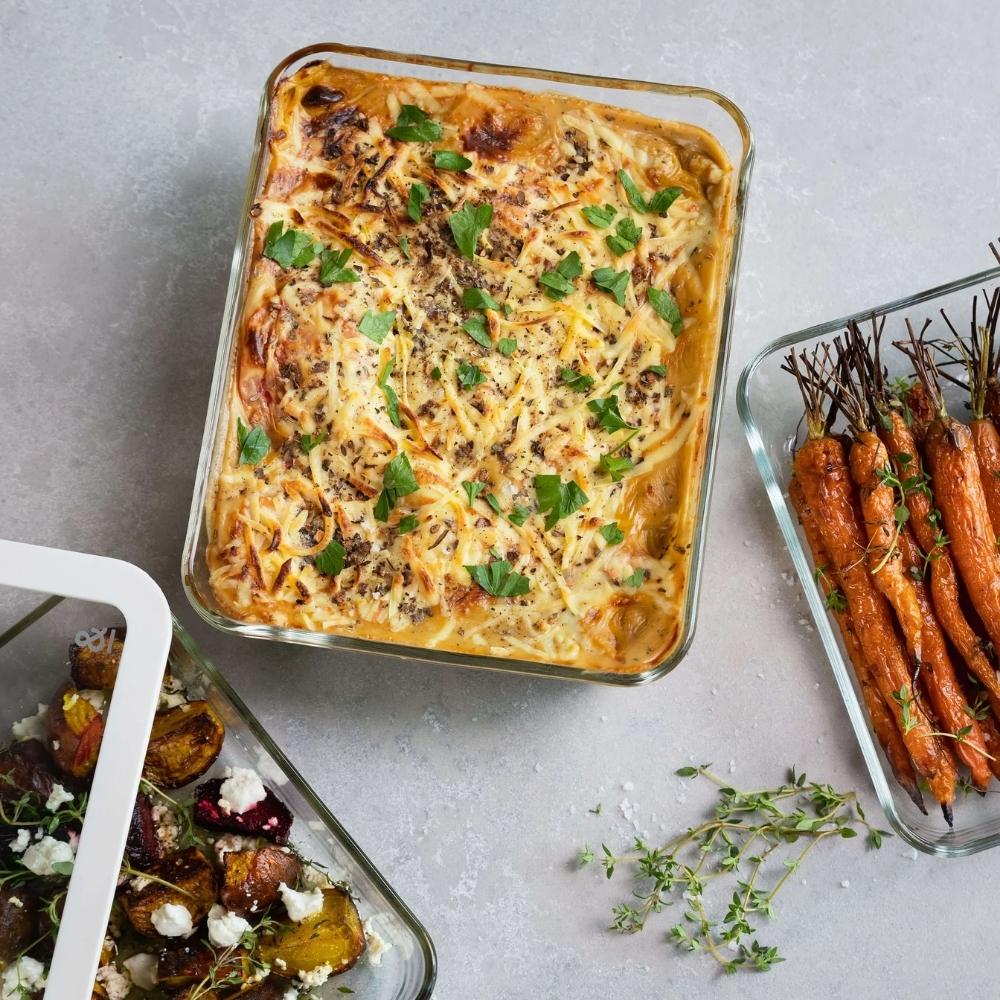 Rektangulære glassbeholdere med glasslokk fra Seed & Sprout fylt med ovnsretter og grønnsaker, brukt til matlaging og servering.
