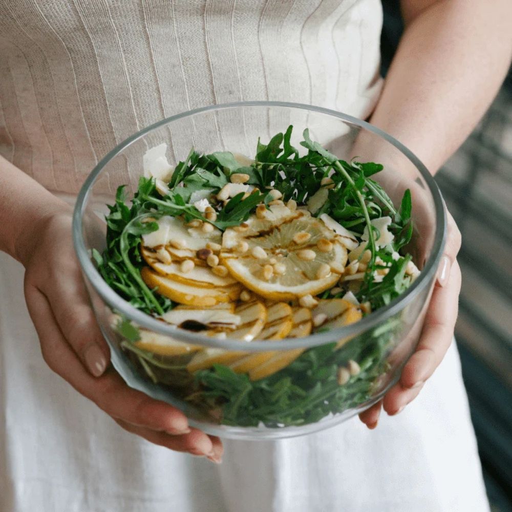 Person som holder en rund glassbolle med frisk salat i en borosilikatglass-beholder fra Seed & Sprout.