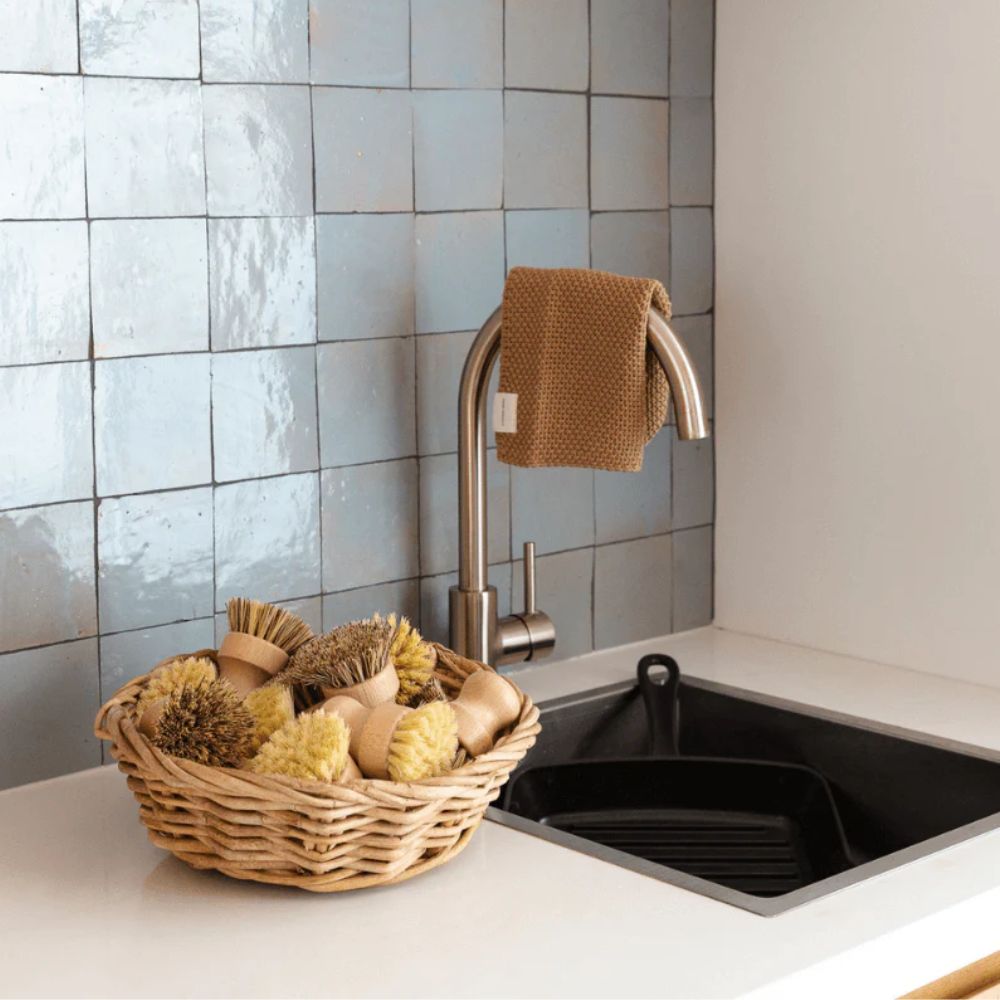 Plastfrie gryteskrubber i bøk og plantefiber samlet i en kurv på kjøkkenbenk ved vask.
