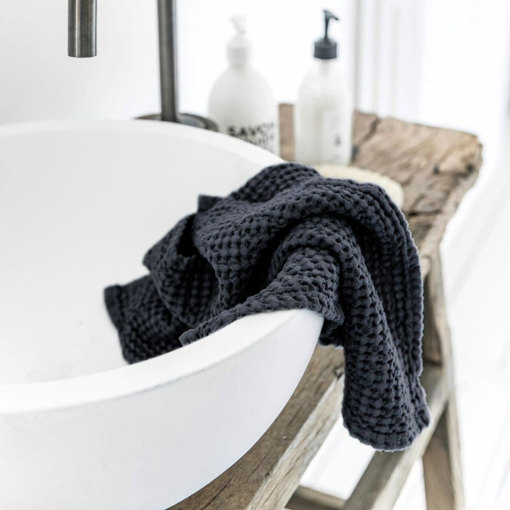Luksuriøst mørkegrått håndkle i lin og bomull henger på bad med naturlige detaljer. Vaffelstruktur gir spa-følelse, rask tørketid og et sunt innemiljø