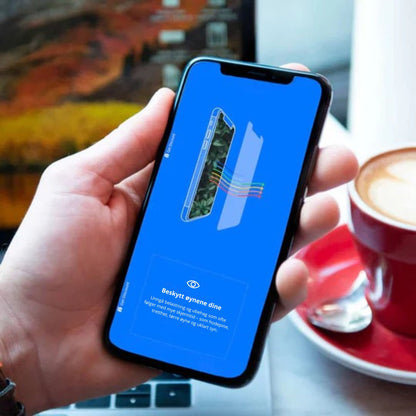 Hånd som holder iPhone med Ocushield skjermbeskytter – teksten på skjermen lyder: "Beskytt øynene dine: unngå belastninger og ubehag som ofte følger med mye skjermtid