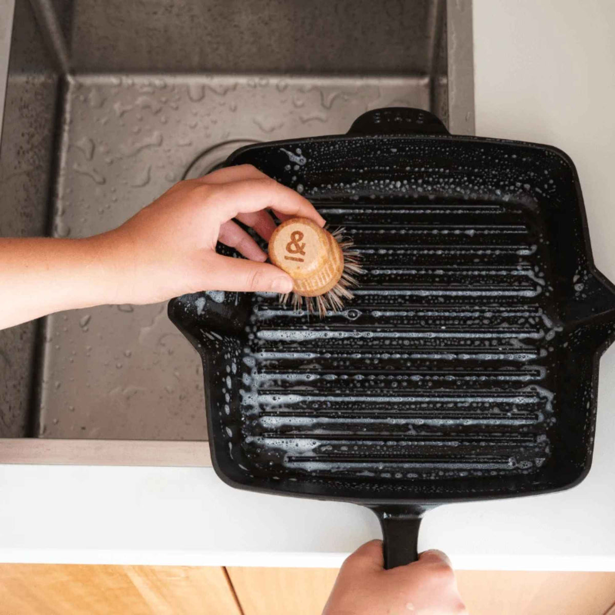 En kraftig gryteskrubb brukes til å vaske en rillet grillpanne med oppvaskmiddel