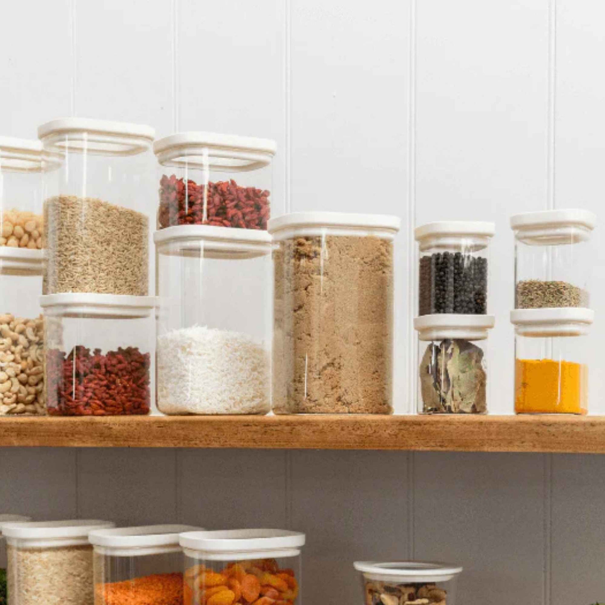 Krydderglass og glassbeholdere med glasslokk fylt med krydder og tørrvarer organisert på kjøkkenhylle.