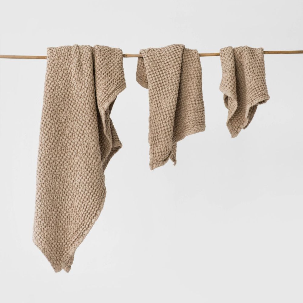 Badehåndkle, håndhåndkle og ansiktshåndkle i beige lin og bomull hengende på snor, luftige og naturlige tekstiler som tørker raskt