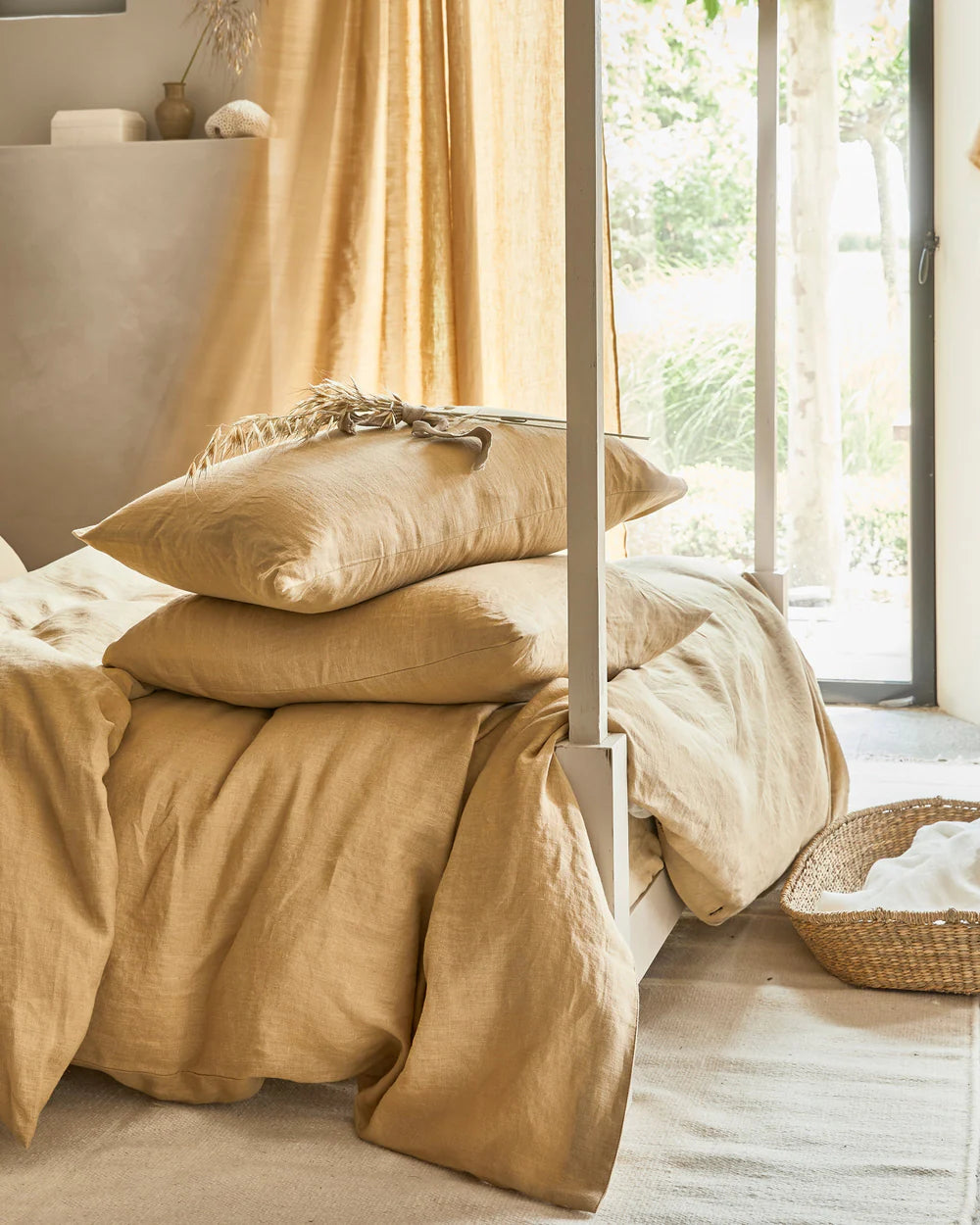 Beige lin sengetøy i lin og bomull med stablede puter i lyst soverom med naturlige materialer