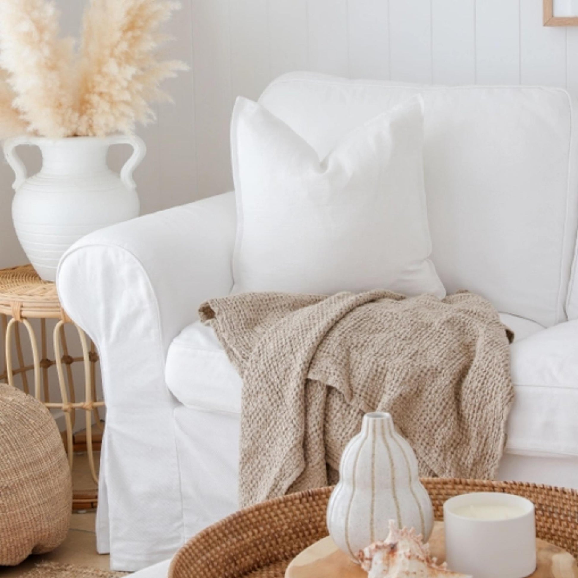 Beige linpledd i vaffelvev drapert over en sofa i en lys, naturlig stue, som viser den myke, steinvaskede teksturen.