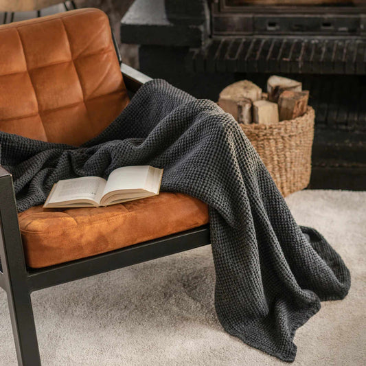 Luksuriøst mørkegrått pledd i lin og bomull, elegant plassert over en stol, perfekt for et sunt og bærekraftig hjem.