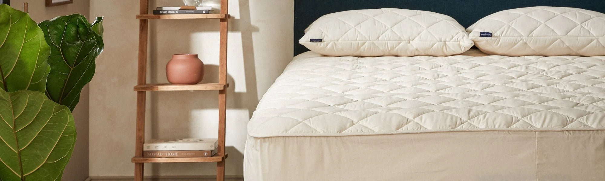 Seng med madrassbeskytter i ull og bomull i naturlig soverom brukt som illustrasjon til guide om valg av madrassbeskytter.
