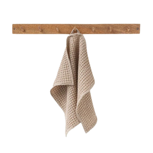 Beige ansiktshåndkle i vaffelvevd lin og bomull fra MagicLinen hengende på en knagg på badet. Pustende og naturlig tekstil som tørker raskt og gir et sunt og hygienisk hjemmemiljø.