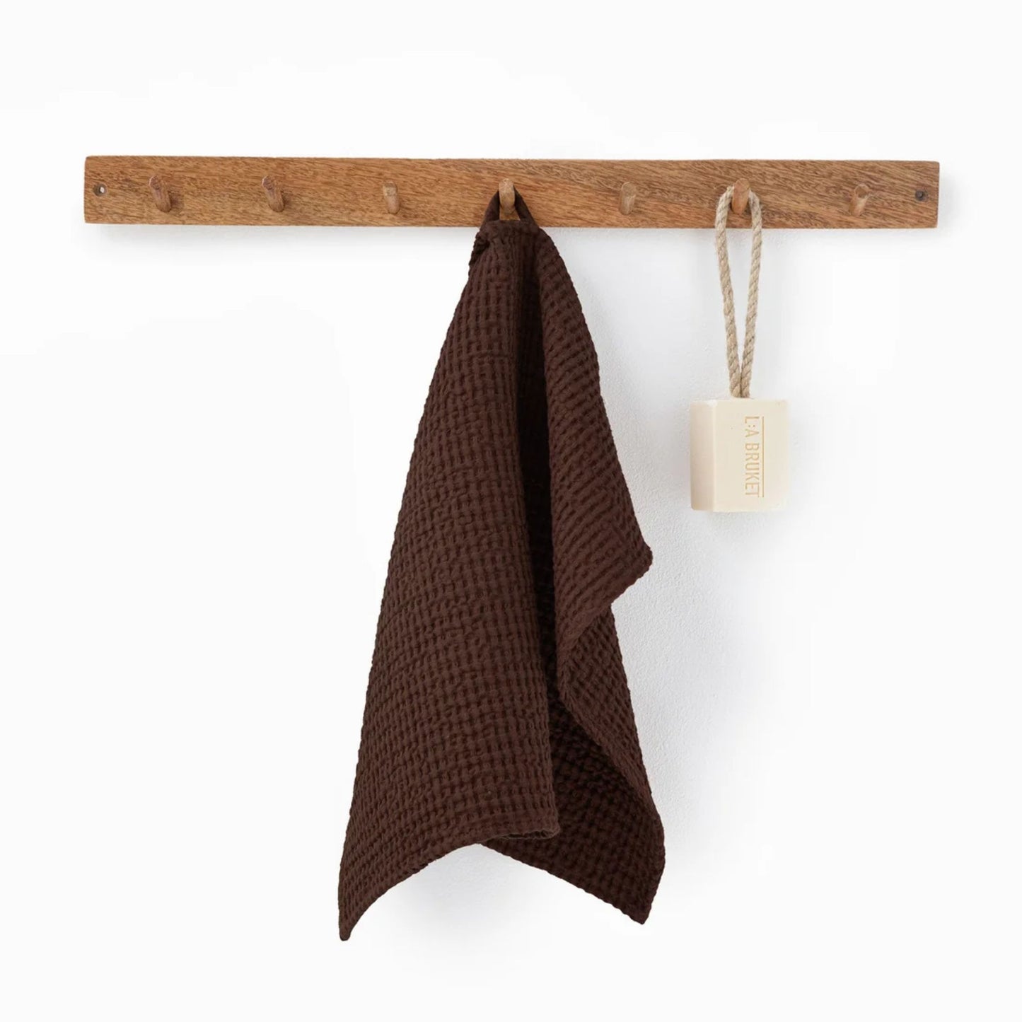 Dark Chocolate ansiktshåndkle i vaffelvevd lin og bomull fra MagicLinen, hengende på en trekrok på badet.