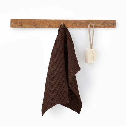 Dark Chocolate ansiktshåndkle i vaffelvevd lin og bomull fra MagicLinen, hengende på en trekrok på badet.