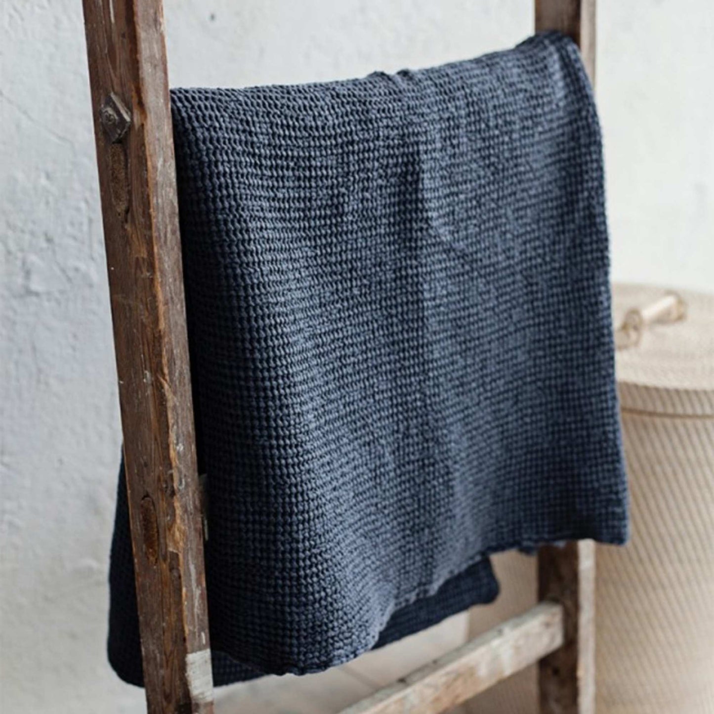 Mørkegrå waffle-pledd i lin og bomull hengende, viser den luftige vaffelstrukturen og naturlige fargetonen.