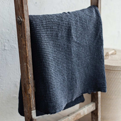 Mørkegrå waffle-pledd i lin og bomull hengende, viser den luftige vaffelstrukturen og naturlige fargetonen.