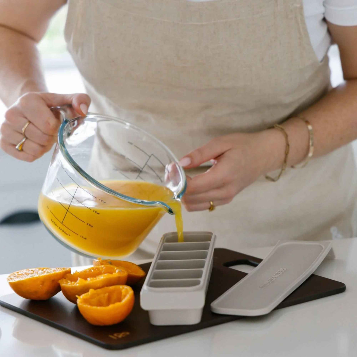 Glasskannen fra sitruspressen brukes som målebeger til å helle fersk appelsinjuice i en silikonfryseform.