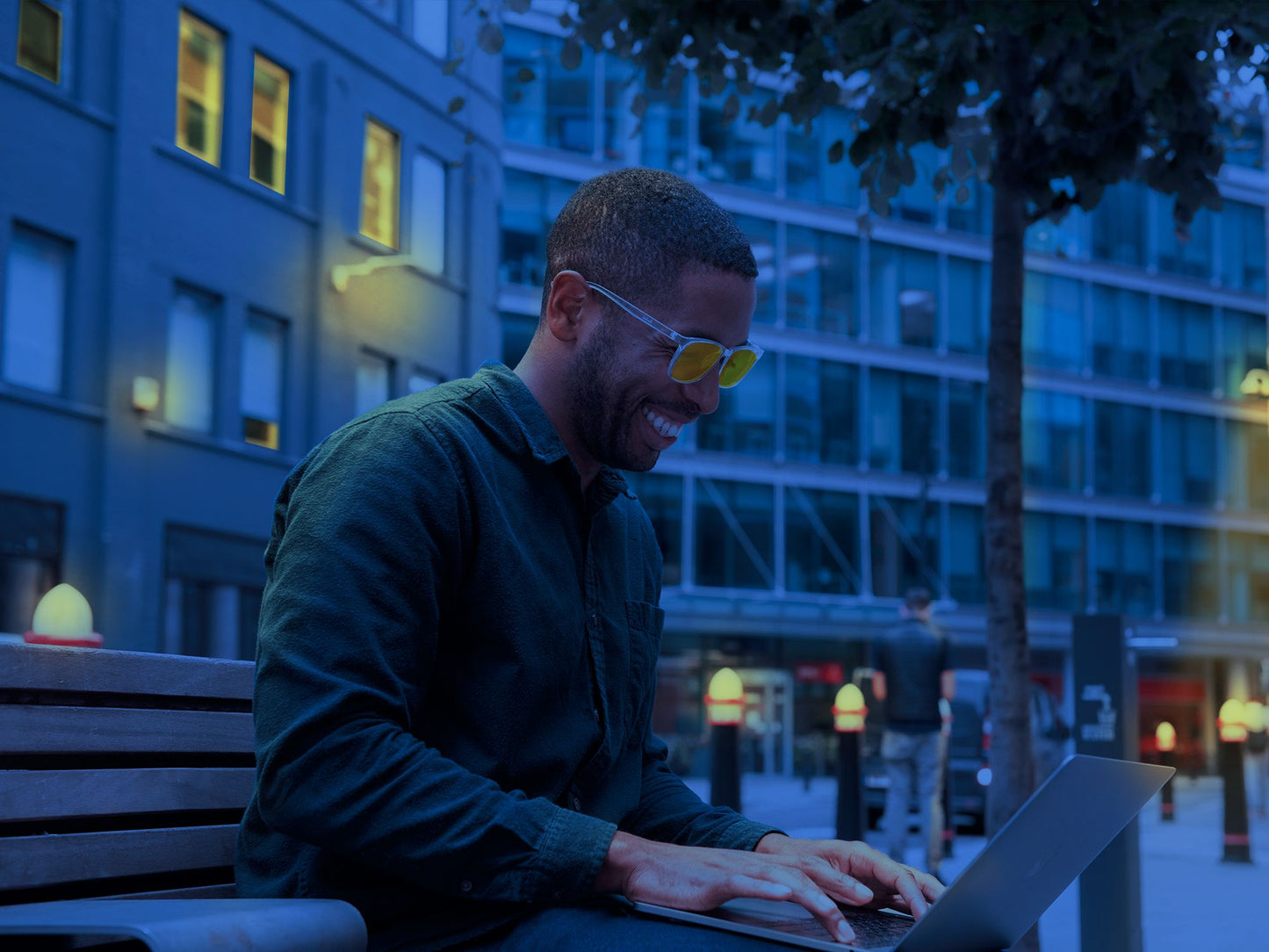 Mann utendørs på kvelden foran dataskjerm med Ocushield Parker blålysbriller med klar innfatning og oransje glass for skjermbruk og bedre søvn