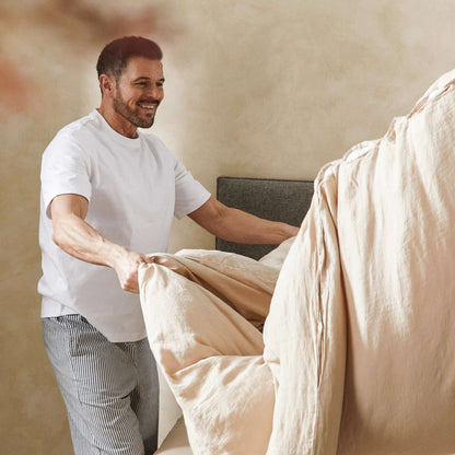 Rolig morgenstemning der en mann rer opp sengen med bærekraftig sengetøy i lin og økologisk bomull