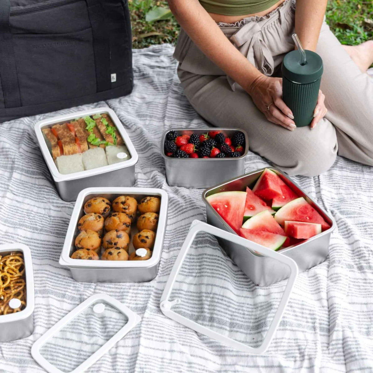 Matbeholdere i rustfritt stål med glasslokk brukt til piknik med frukt, bær og annen mat.