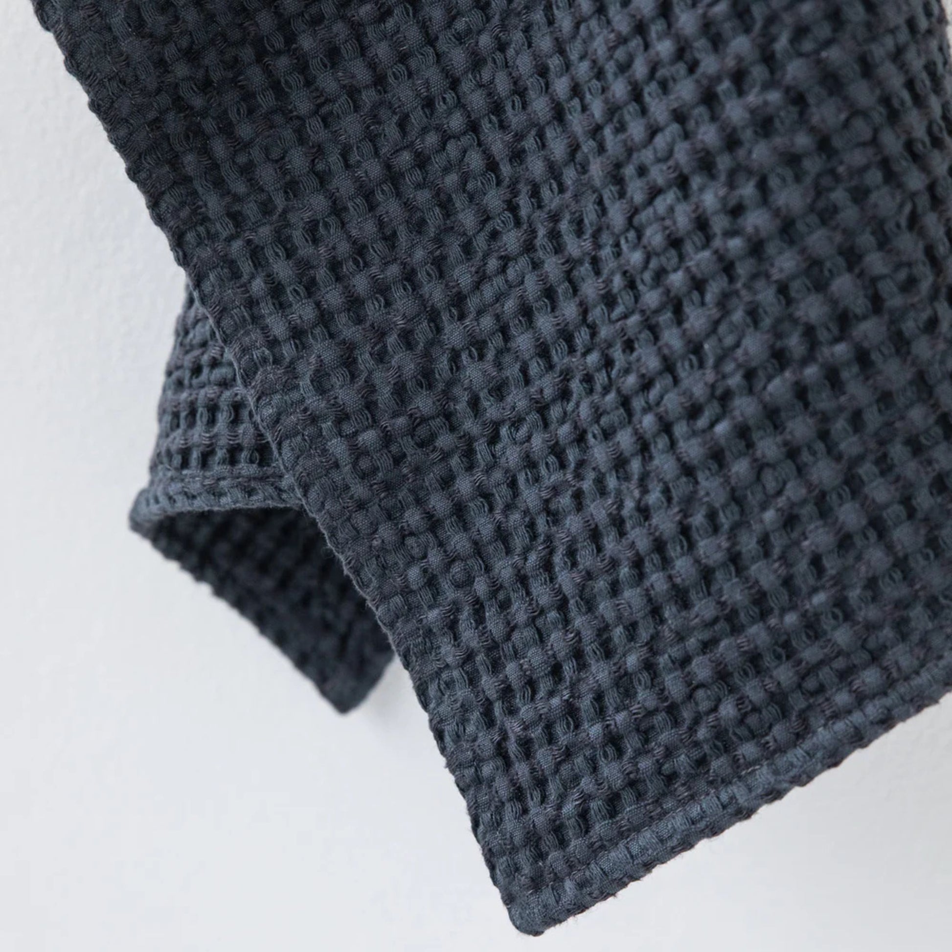 Nærbilde av vaffelvev i mørkegrått ansiktshåndkle laget av lin og bomull fra MagicLinen. Viser den luftige strukturen som gir rask tørk, god absorbering og skånsom eksfoliering for sensitiv hud