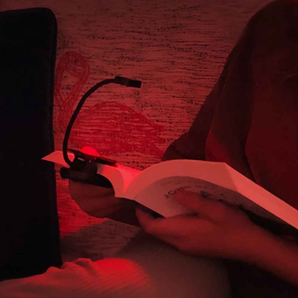Person leser i sofaen med NoBlue leselampe festet på boken og dempet rødt lys