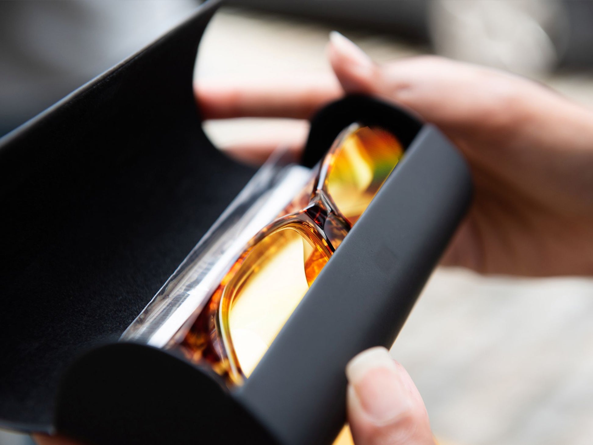 Ocushield Parker blålysbriller med oransje glass i brilleetui, holdt i to damehender